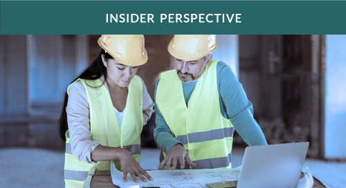 A woman and man in hard hats looking over architectural plans at a building site.