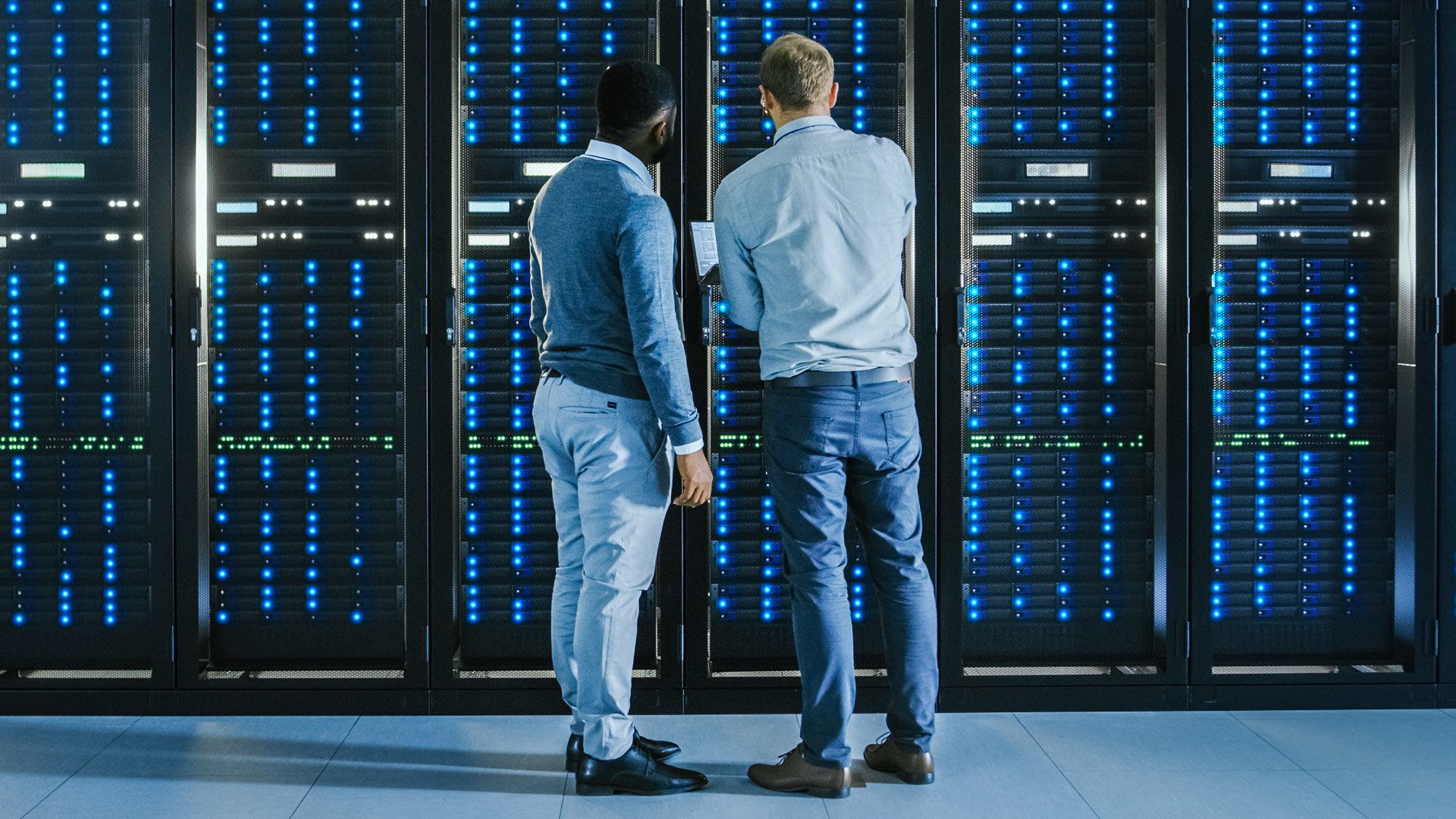 Two people standing in front of a generic server rack meant to convey AWS.